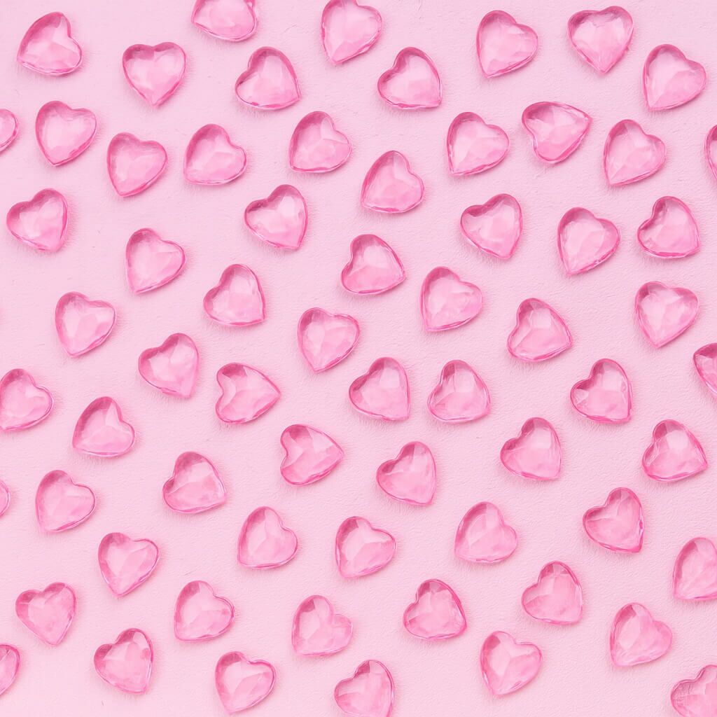 Lyserøde hjerteformede pynte diamanter spredt på en lyserød baggrund.
