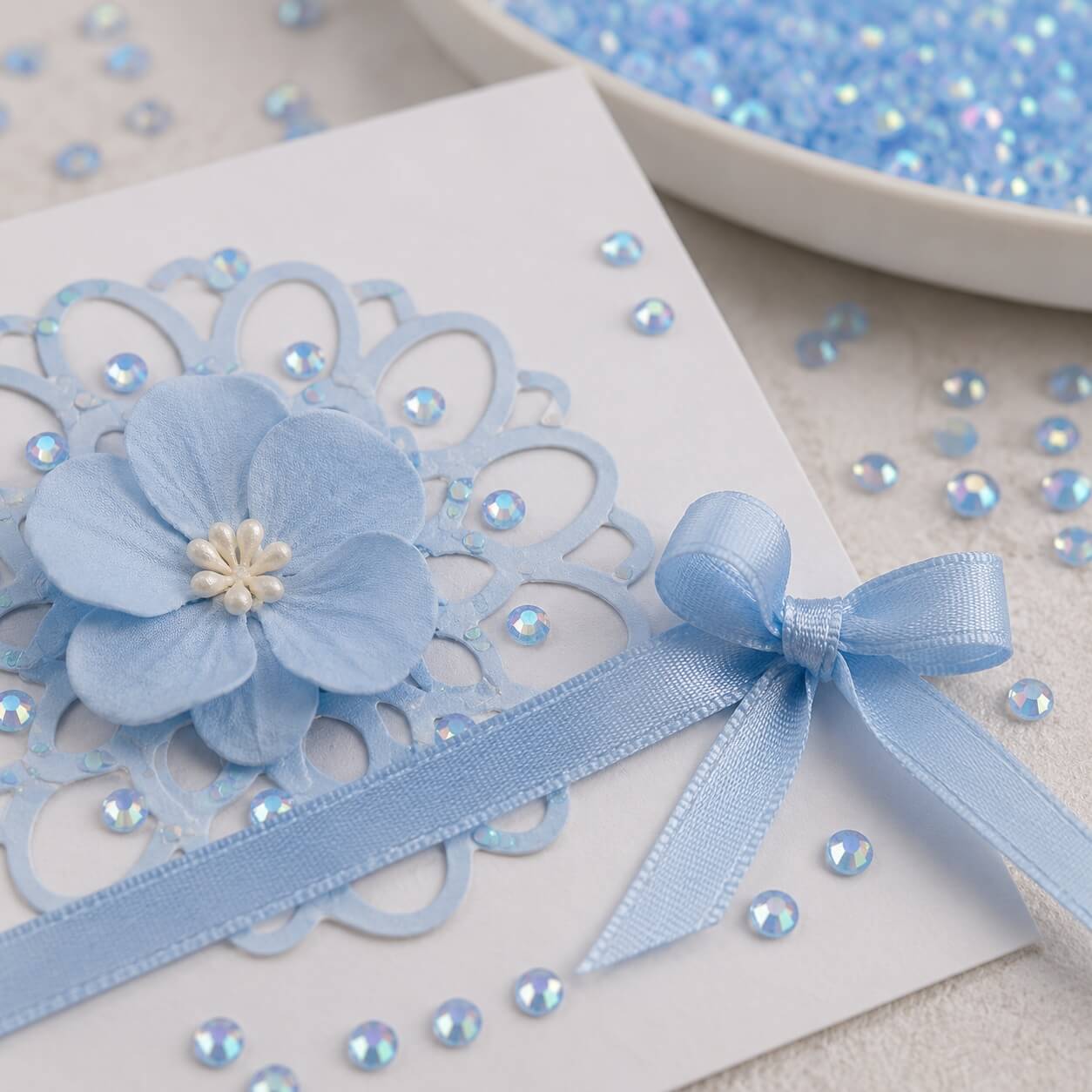 Rhinsten 6 mm iriserende lyseblå anvendt på håndlavet kort med satinbånd og papirblomst til scrapbooking og kortfremstilling.